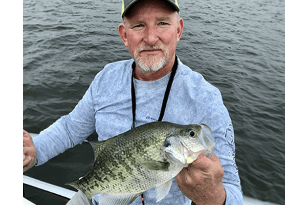 A man holding a fish while standing on top of a boat.